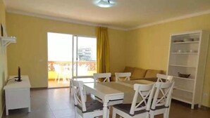 A dining area with a white table and chairs, a sofa, and a white shelving unit. - APCOSTAS Quijote / Two Bedrooms (L'Estartit)