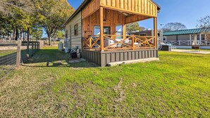 A wooden cabin with a porch, surrounded by a fenced area and trees. - New-Build Waterfront Cabin, Lake Conroe (Willis)
