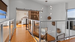 Habitación de hotel moderna con piso de madera, balcón de vidrio y un amplio ventanal con vista a la ciudad.