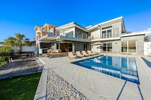 A modern two-story house with a swimming pool, outdoor seating, and a well-maintained lawn.