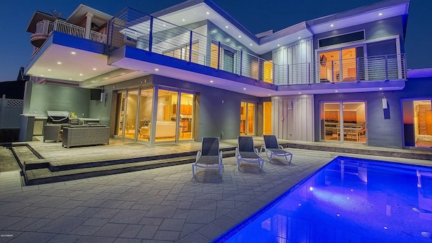 Una casa moderna de dos pisos con piscina, mobiliario exterior y un balcón.
