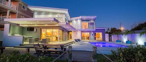 Una casa moderna de dos pisos con piscina, mobiliario exterior y un patio bien iluminado.