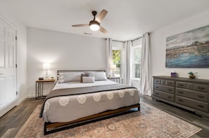 A bedroom with a bed, a nightstand, a dresser, a ceiling fan, and a painting on the wall. - THE DULUTHIAN (Little Rock)