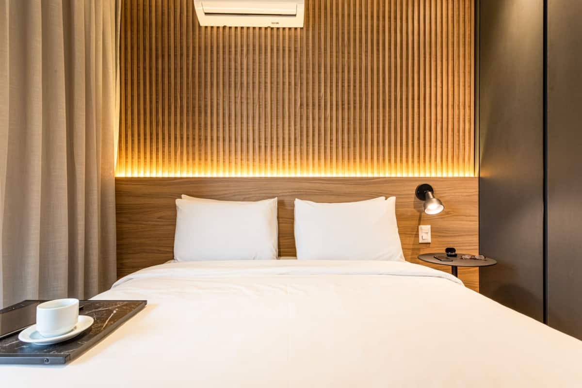 Ein Hotelzimmer mit einem Holz-Kopfteil, einem Nachttisch mit Lampe und einem Tablett mit Tasse und Untertasse.