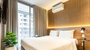 A modern hotel room with a large bed, a potted plant, a bedside table with a lamp, and a view of the city through the window. - Charlie Wide Pinheiros (São Paulo)