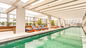 An indoor swimming pool with lounge chairs and potted plants. - Charlie Wide Pinheiros (São Paulo)