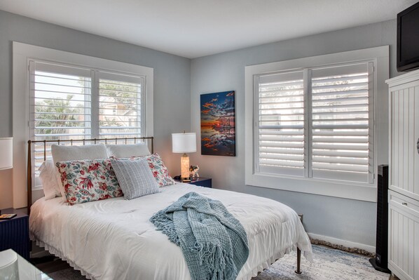 A bedroom with a bed, nightstands, a lamp, a painting, and a television.