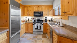A kitchen with wooden cabinets, stainless steel appliances, granite countertops, and a tiled floor.