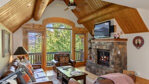 A cozy living room with leather sofas, a stone fireplace, and a television mounted on the wall.