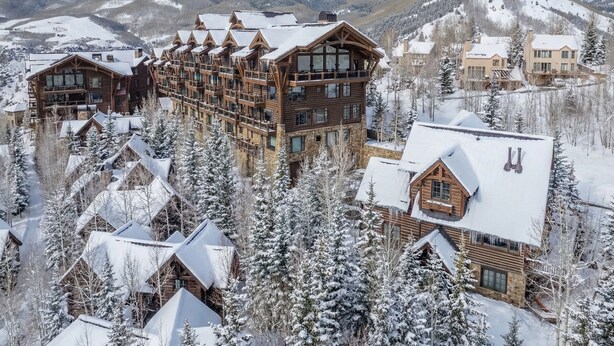 A lodge with multiple wooden buildings, snow-covered trees, and a mountainous backdrop.
