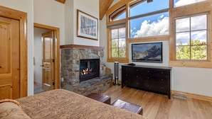 A cozy room with a stone fireplace, wooden ceiling, and large windows offering a mountain view.