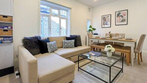 Una sala de estar con sofá, una mesa de centro de vidrio y un comedor con una mesa dispuesta para dos.