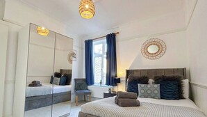Un dormitorio con un espejo grande, una cama con almohadas, una silla y una ventana con cortinas.