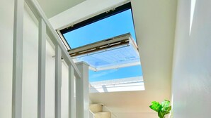 Een trap met dakraam leidend naar een balkon, een bloempot en een zithoek met kussens.