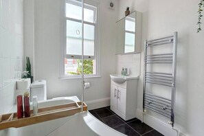 Un baño con bañera, lavamanos, espejo y toallero.