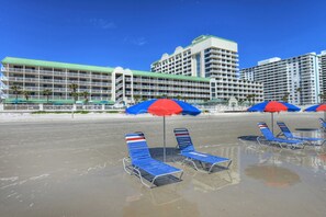 Een hotel aan het strand met meerdere balkons, strandparasols en ligbedden.