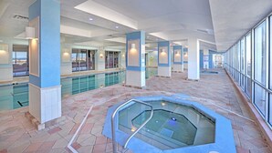 Zona de piscina interior espaiosa amb una banyera d'hidromassatge, grans finestres i un paviment de rajola.