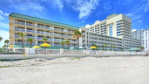 Et strandhotel med flere balkoner, udendørs parasoller og et sandstrandområde.
