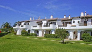 Un edificio blanco con varios balcones y puertas arqueadas, rodeado de un césped cuidado y palmeras.