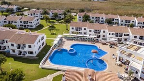 Un resort con piscina central, varias edificaciones blancas con techos de tejas rojas y vistas al océano.