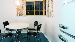 Een eetruimte met een ronde tafel, vier stoelen, een raam met gordijnen en een vintage koelkast.