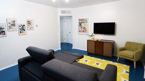 Een moderne woonkamer met een bank, een televisie, een klein kastje en een deur naar een andere kamer.