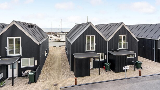 A row of black cabins with white windows, a paved walkway, and a marina in the background. - 2 bedroom gorgeous home in Tranekær (Tranekær)