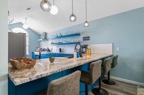 Une cuisine moderne avec des meubles bleus, un comptoir en marbre et des tabourets de bar.