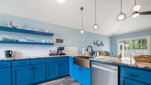 Eine Küche mit blauen Schränken, einer Kaffeebar und einem Fenster mit Blick ins Freie.