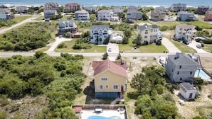 An aerial view of a coastal residential area with houses, a swimming pool, and a road.
