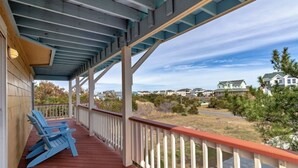 A covered porch with red flooring and white railings, overlooking a residential area with houses and a clear sky.