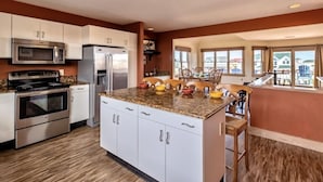 A modern kitchen with stainless steel appliances, a central island with stools, and large windows offering a view of the outside.