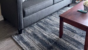 Un salon moderne avec un canapé gris, des coussins décoratifs à motifs, une table basse en bois et une planche de surf accrochée au mur, qui sert d’élément décoratif.