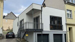 A modern two-story building with a balcony, a garage, and a car parked in front. - Loft with wallbox, WLAN workstation, garage, for 3 people, 100 m to the Moselle (Traben-Trarbach)