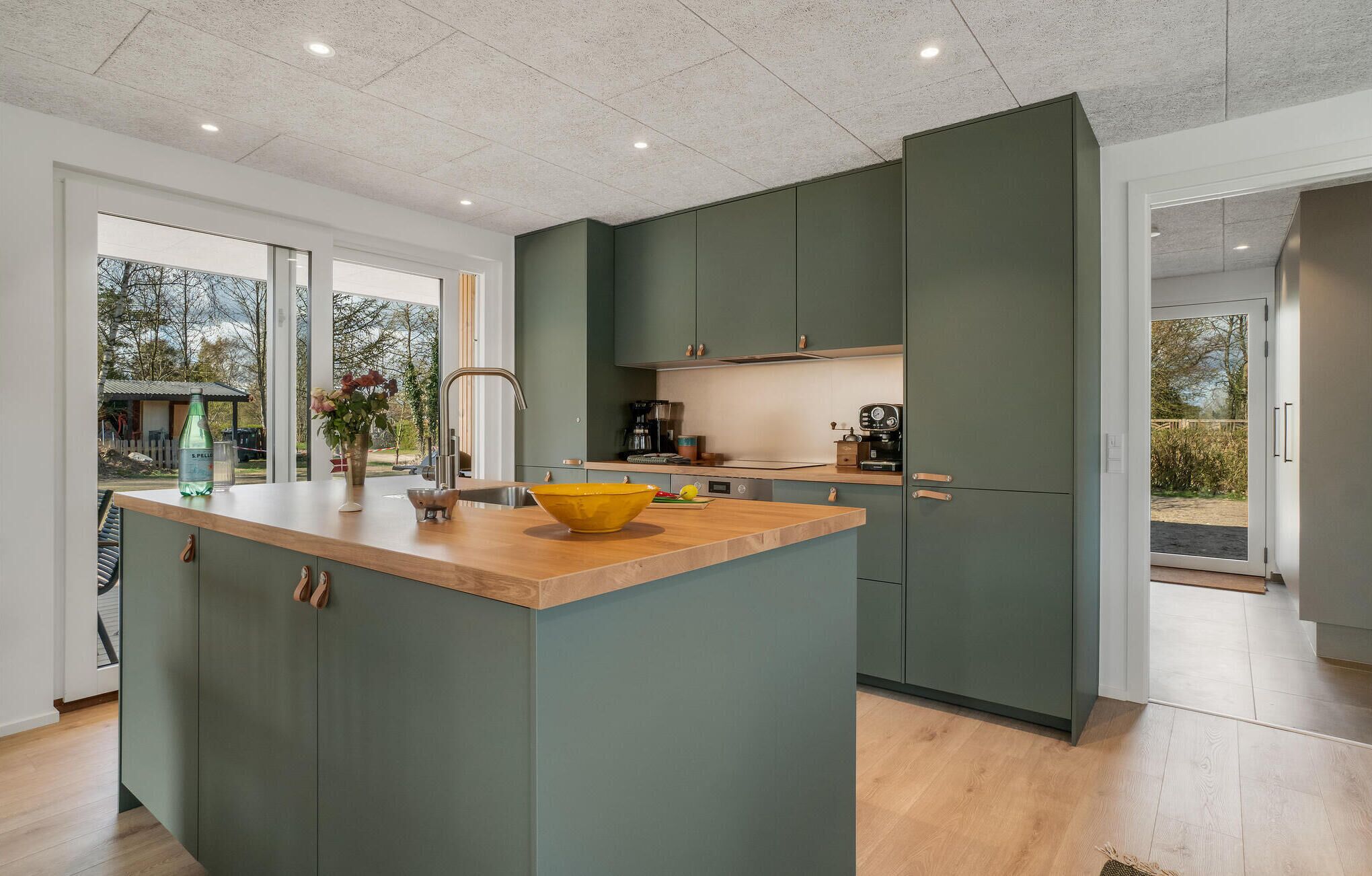 A modern kitchen with a central island, green cabinets, and a view of the outdoors.
