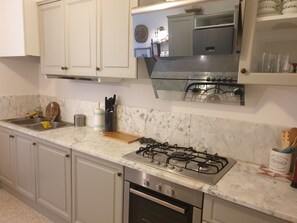 Una cocina con armarios blancos, un lavamanos de acero inoxidable, una estufa a gas y un horno empotrado.