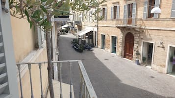 Una stretta via acciottolata fiancheggiata da edifici, con tavolini all'aperto e qualche vaso di piante.