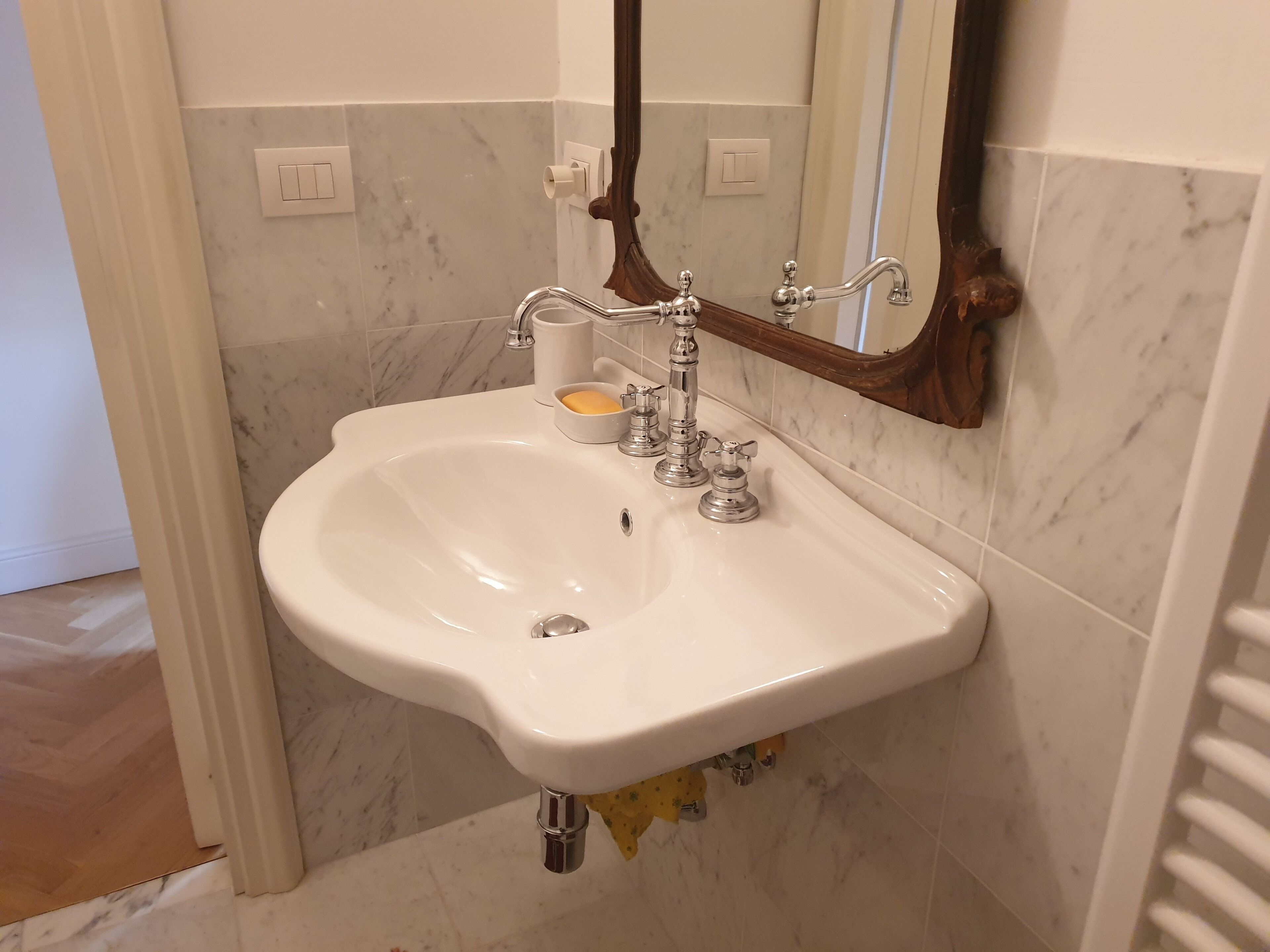 A bathroom with a white sink, a mirror, and a marble-tiled wall.