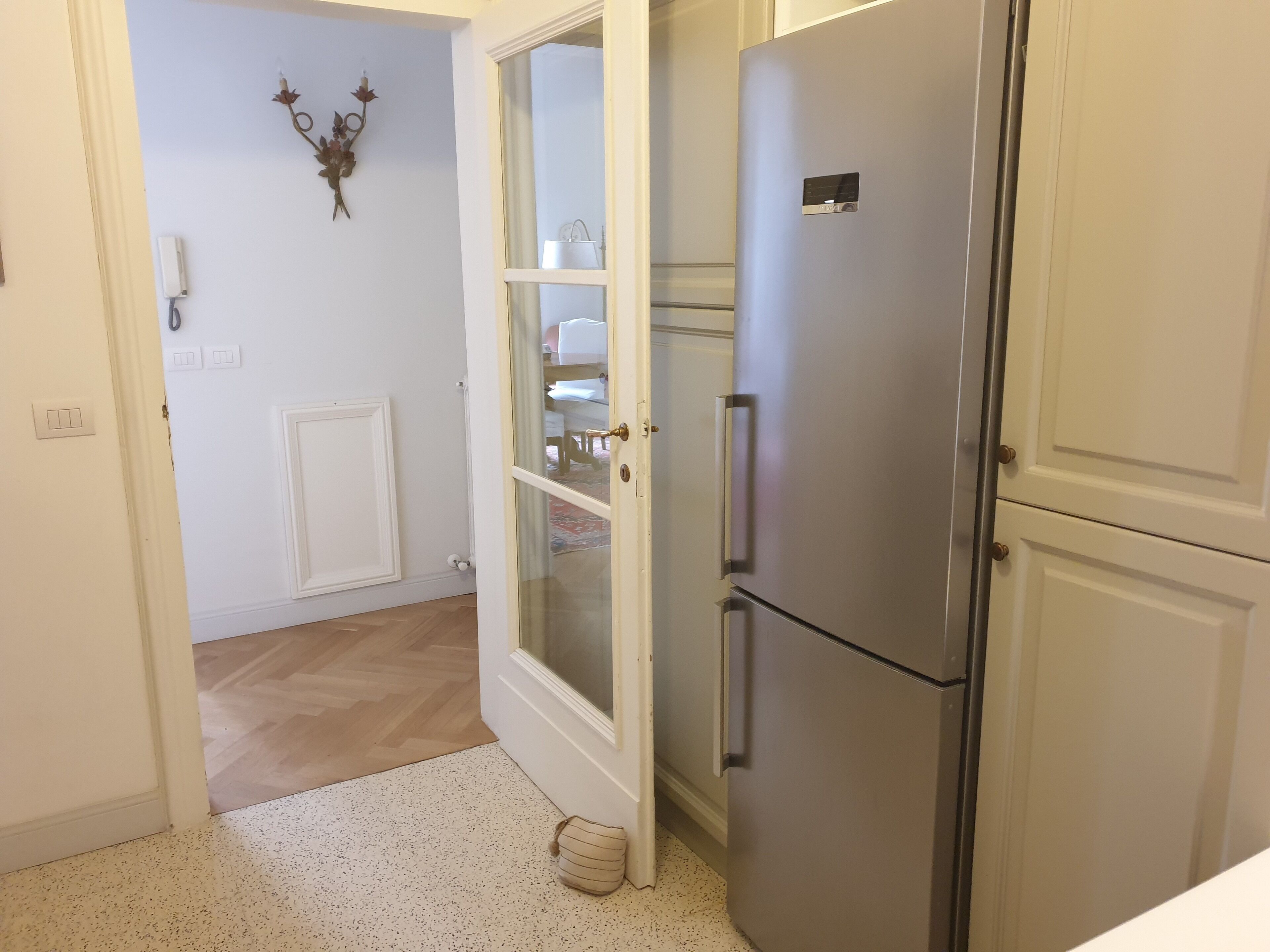 Cucina con frigorifero in acciaio inossidabile, una porta bianca con vetrate e un elemento decorativo a parete.