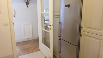 Cucina con frigorifero in acciaio inossidabile, una porta bianca con vetrate e un elemento decorativo a parete.