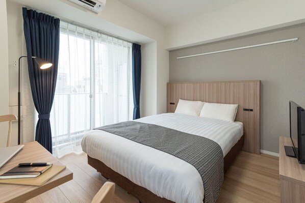 Relax in a cozy space with a neatly made bed, desk for work, and a TV for entertainment.