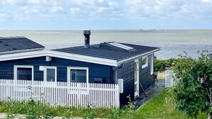 Uma casa costeira com cerca branca, fachada azul escura e vista para o mar.