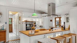Ett kök med vita skåp, en köksö i trä med barstolar, en grön hänglampa och ett stort fönster.