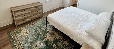 Un dormitorio con cama, ventilador de techo, ventana con persianas, banca de madera y puerta que da a un baño.