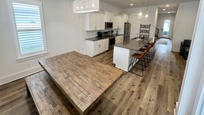 A modern kitchen with white cabinets, a central island with bar stools, and a wooden dining table. - Spacious, 4BR Beach Home with Golf Cart & Pool Access (Miramar Beach)