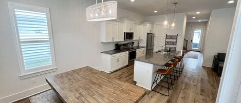 A modern kitchen with white cabinets, a central island with bar stools, and a wooden dining table.