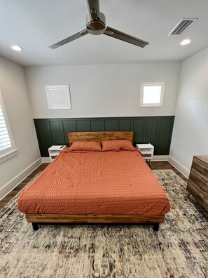 A bedroom with a bed, a ceiling fan, two bedside tables, a dresser, and a window with blinds.