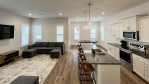 A modern kitchen with a central island, bar stools, and stainless steel appliances. - Spacious, 4BR Beach Home with Golf Cart & Pool Access (Miramar Beach)