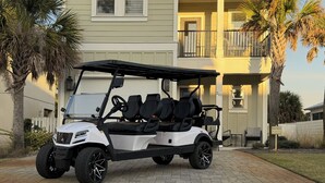 A white golf cart parked on a paved driveway in front of a two-story house with a balcony. - Spacious, 4BR Beach Home with Golf Cart & Pool Access (Miramar Beach)