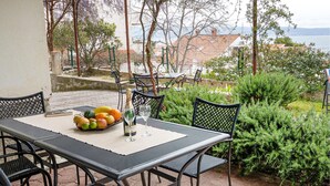 Patio esterno con tavolo apparecchiato per due persone, con una bottiglia di Heineken, un bicchiere e un cesto di frutta.